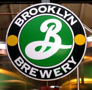 A circular Brooklyn Brewery logo with a green center, a white script "B," and two yellow dots.