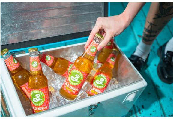 Hand reaching into a cooler filled with ice and bottles of Brooklyn Brewery Playa de Brooklyn Lime Lage