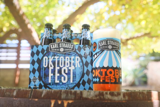 Karl Strauss Oktoberfest beer six-pack and glass, featuring the distinctive blue and black checkered label design