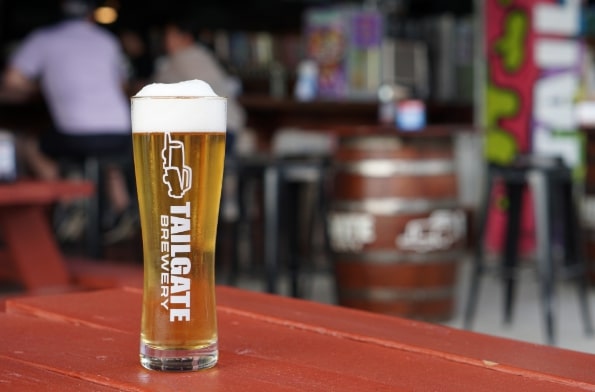 A glass of Tailgate Brewery beer on a wooden table inside a vibrant brewery taproom