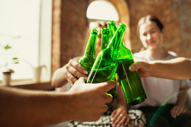 Group of young students clinking green bottles of alcohol-free beer in a casual indoor setting