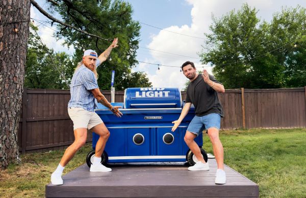 NFL stars, George Kittle and Baker Mayfield pose with a blue Bud Light branded Traeger grill in a backyard setting