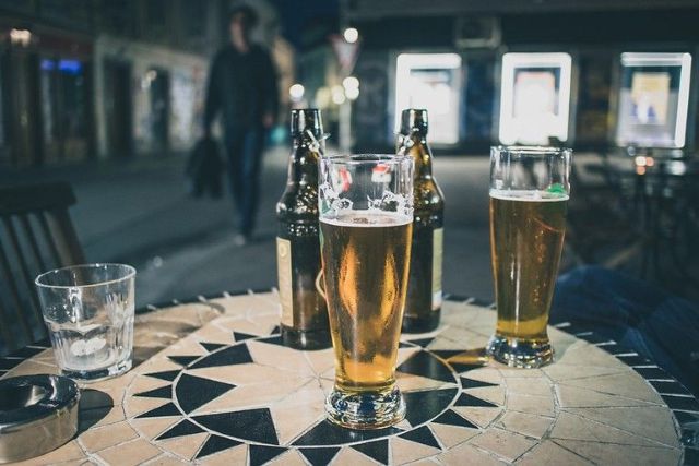 Glasses and bottles of craft beer on a patterned outdoor table at night