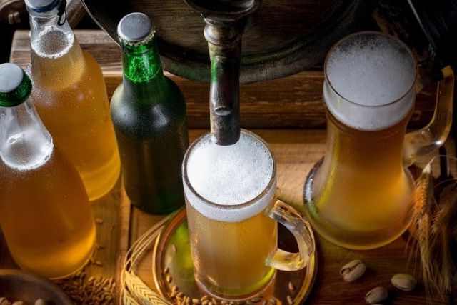 Cold craft beers being poured from a rustic tap surrounded by bottles and brewing grains, reflecting the artisanal process behind fermentation science.