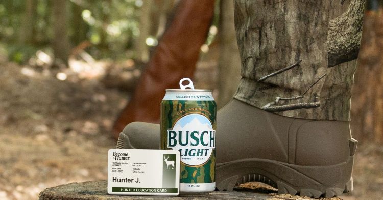 An image of a Busch Light Collector's Edition beer can featuring a camouflage design, placed on a tree stump next to a "Become Hunter" Hunter Education Card belonging to "Hunter J." and a person wearing a camouflage hunting boot in a wooded outdoor setting.