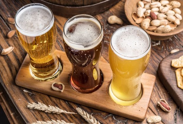 "Craft beer flight on a wooden table with three distinct beers, roasted peanuts, and wheat stalks
