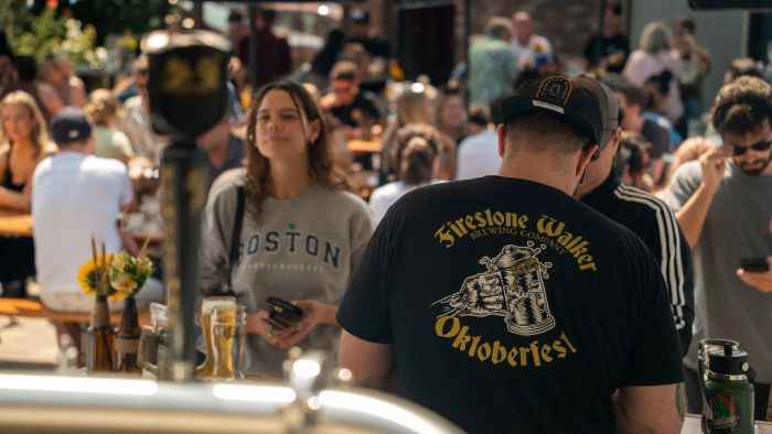 Oktoberfest celebration featuring attendees, including one person wearing a "Firestone Walker Brewing Company Oktoberfest" t-shirt, at an outdoor event