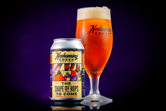 Neshaminy Creek The Shape of Hops to Come Imperial IPA beer can and a branded glass filled with golden beer against a dark background.