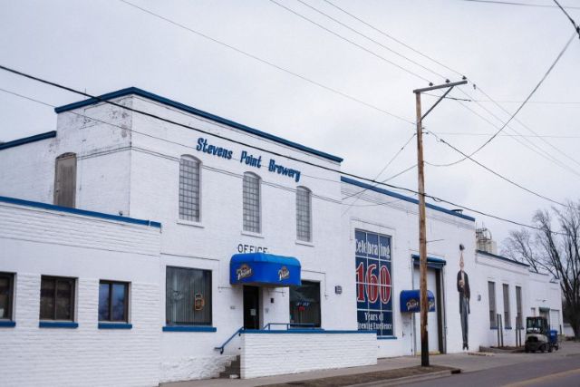 Stevens Point Brewery exterior in winter, featuring the iconic white building with blue trim, "OFFICE" sign, and "Celebrating 160 Years" banner