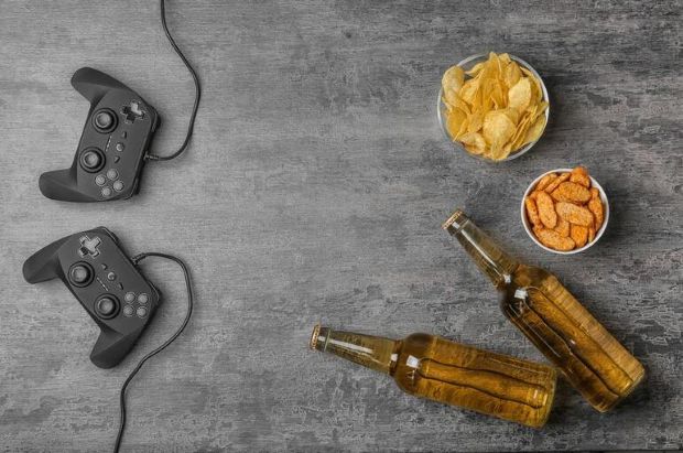 Beer bottles, snacks, and video game controllers on a grey background