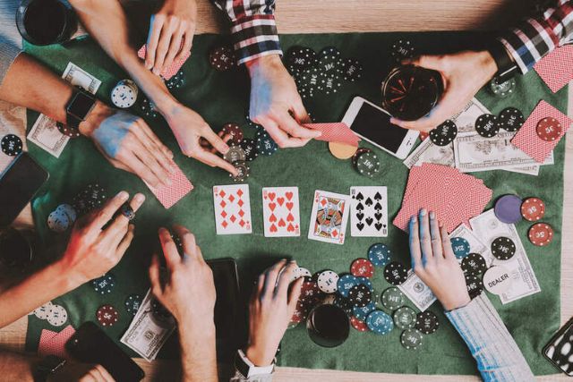 Group of people playing poker with cards, chips, and smartphones on a green felt table
