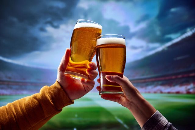 Fans clinking beer glasses at a football stadium, representing NFL 2025 beer prices
