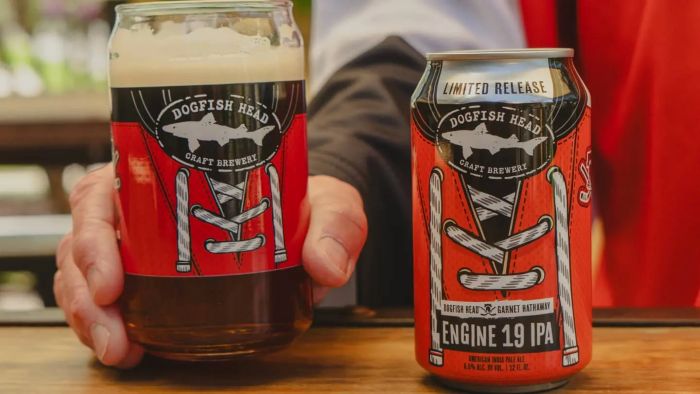 A limited release Dogfish Head Engine 19 IPA beer, shown in both a branded can with a distinctive shoelace design and a glass filled with the amber craft beer, held by a hand.