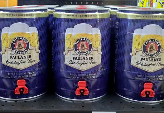 Paulaner Oktoberfest Bier 5L mini kegs with red taps on a store shelf, featuring the "IMPORTED FROM GERMANY" label
