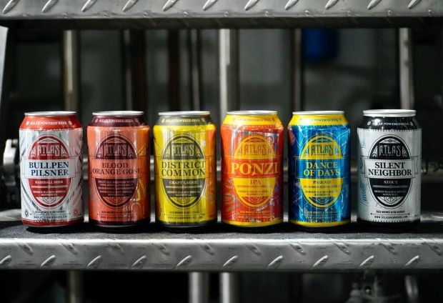Six cans of Atlas Brew Works beer are lined up on a metal grate. The cans are, from left to right, Bullpen Pilsner, Blood Orange Gose, District Common, Ponzi IPA, Dance of Days, and Silent Neighbor.