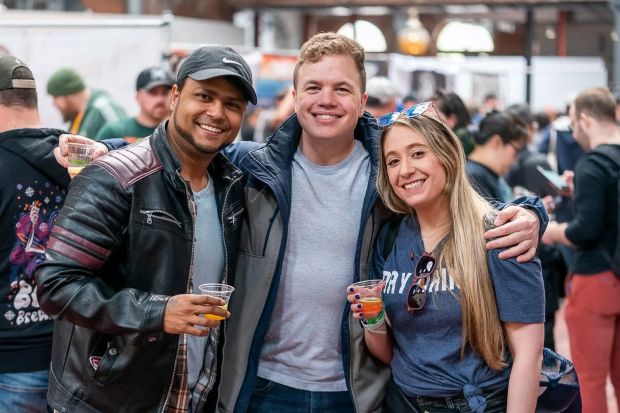 Three friends smiling and holding small glasses at Mass Brewers Guild conference.