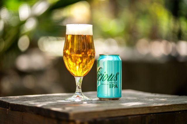 Stone Delicious Tropical IPA in a glass next to the can on a wooden table