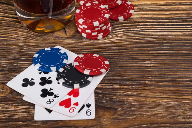 Poker chips and playing cards on a wooden table next to a glass of beer
