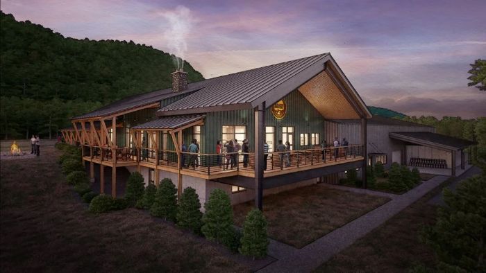 A modern, lodge-style brewery building with a large wraparound deck is illuminated at dusk.