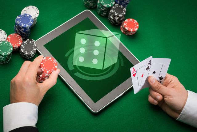 Person playing online casino games on a tablet with poker chips and cards on a green table