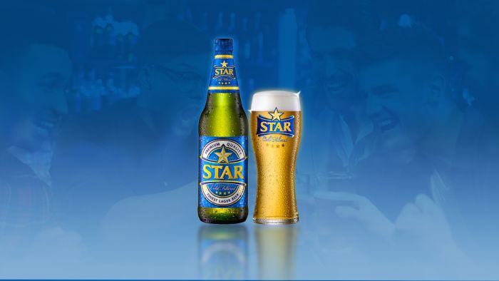 A bottle of Star lager beer next to a glass of the same beer against a blue background.