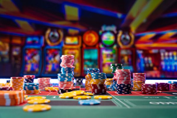 Colorful casino chips stacked on a roulette table with slot machines glowing in the background at Lucky Owl Club Casino Australia.