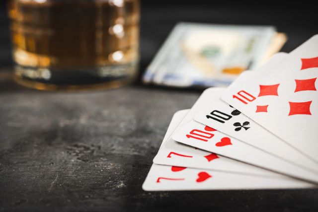 Poker hand with sevens and tens on a dark table, with cash and a glass of beer in the background.