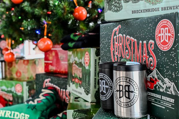 boxes of Breckenridge Brewery Christmas Ale and two branded koozies, set against a backdrop of a decorated Christmas tree and wrapped gifts.