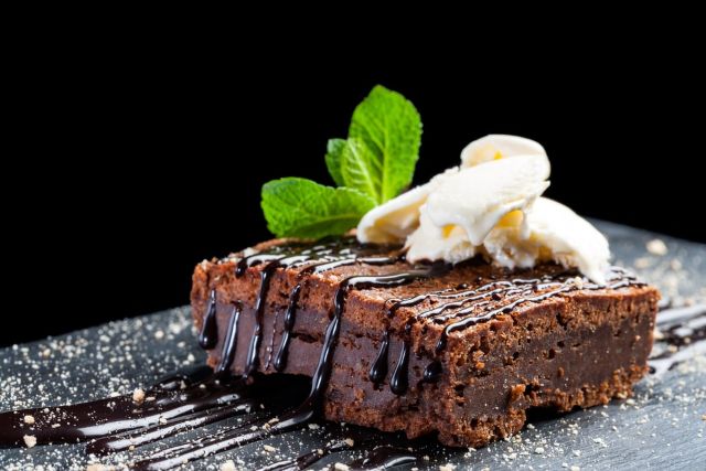 A rich chocolate brownie topped with scoops of vanilla ice cream, a chocolate drizzle, and a sprig of fresh mint.