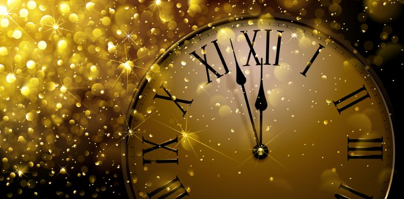 A clock face with Roman numerals showing the time close to midnight, set against a background of shimmering gold lights suggesting a festive occasion such as New Year's Eve.