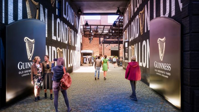 People walking through a long entrance at the Guinness Open Gate brewery in London, with bold Guinness branding and harp logos on the walls.