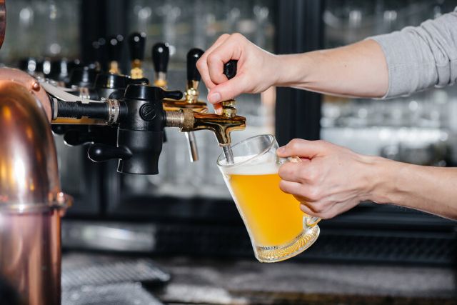 Bartender pouring craft beer into a glass mug at a bar using a tap.