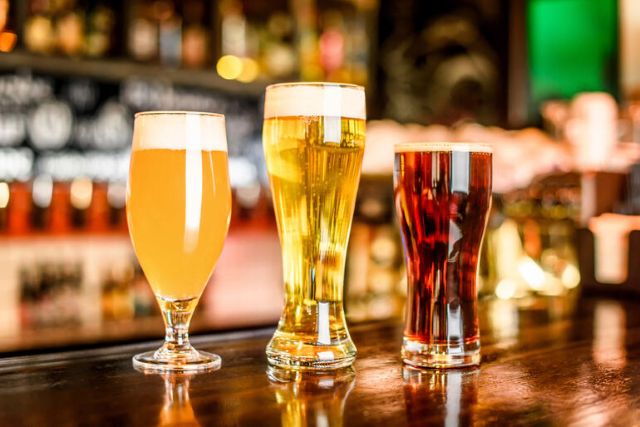 Three different styles of craft beer, light, golden, and dark, served in glasses on a bar, representing America’s underrated beer cities.