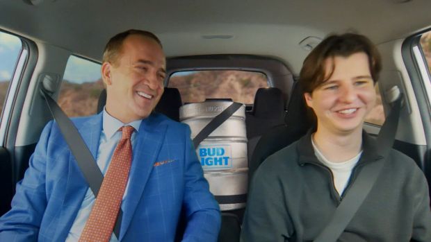 Pro Football Hall of Famer Peyton Manning  being driven in a car, with a keg of Bud Light strapped into the back seat