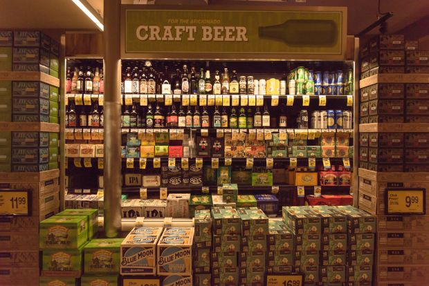 A fully stocked refrigerated display case in a grocery store, featuring a wide selection of bottled and canned craft beers.