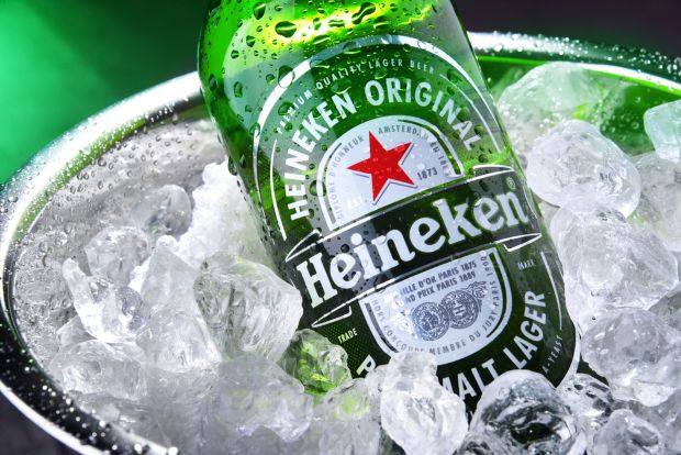 A Heineken beer bottle chilling in a metal bucket filled with ice cubes.