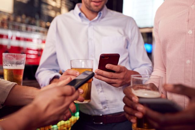 People checking mobile apps and websites while enjoying beer at a bar between rounds