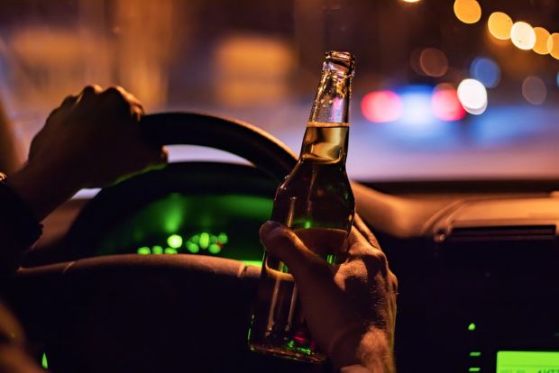 Craft beer enthusiast holding a beer bottle while driving at night, highlighting the risks of drinking and driving.