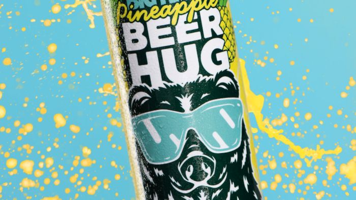 A can of Pineapple Beer Hug beer featuring a black bear wearing sunglasses logo on a blue background with yellow splashes.