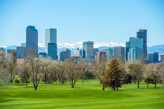 Denver skyline viewed from a green park with snow-capped mountains in the background.