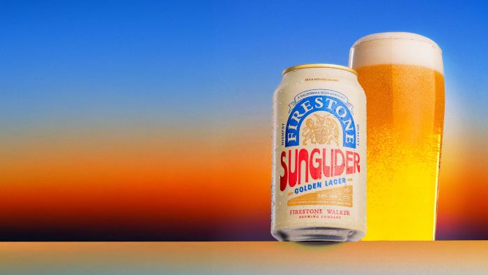 A can of Firestone Walker Sunglider Golden Lager stands next to a tall, foaming glass of beer against a vibrant sunset-colored background.