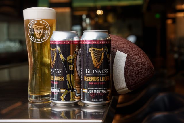 Two cans of Guinness Legends Lager and a glass of the beer are pictured alongside an American football. The limited-edition pale wheat lager was released ahead of Super Bowl LX in collaboration with NFL Hall of Famer Joe Montana to benefit the SF-Marin Food Bank.