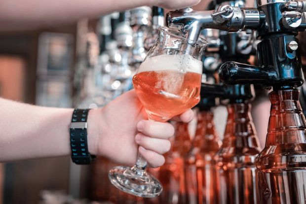 Bartender pouring fresh craft beer from a tap into a glass at a small-town brewery.
