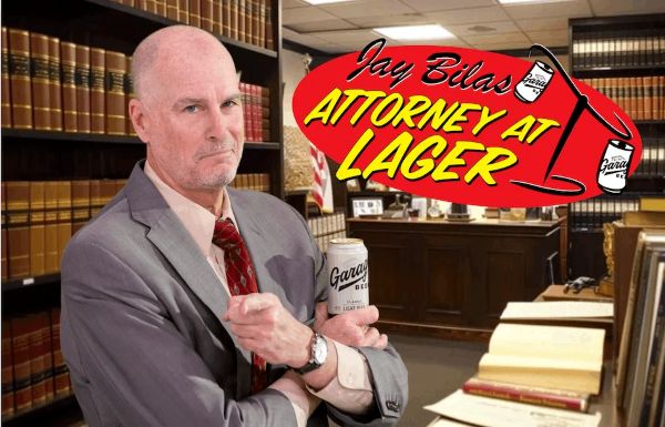 Jay Bilas, dressed as an attorney in a suit and tie, stands in a law library holding a can of Garage Beer, with a logo reading "Jay Bilas: Attorney at Lager."