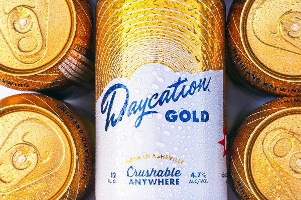 Close-up of several gold beer cans with condensation, featuring a central can labeled "Daycation GOLD" from Highland Brewing.