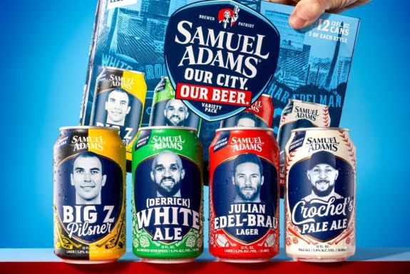 Four Samuel Adams beer cans from the "Our City. Our Beer." variety pack, each featuring a black-and-white portrait of a Boston sports star: Zdeno Chara (Big Z Pilsner), Derrick White (White Ale), Julian Edelman (Edel-Brau Lager), and a baseball player, Garrett Crochet (Pale Ale).