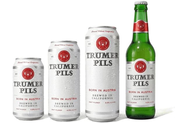 Four various-sized containers of Trumer Pils beer, including three silver cans of increasing height and one green glass bottle, arranged in a row