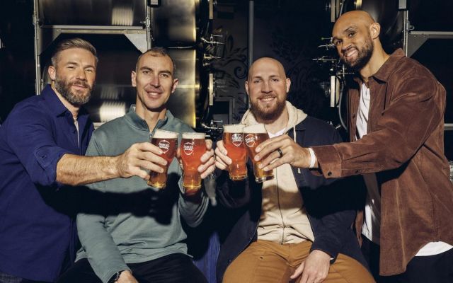 Four men smiling and posing for a photo while holding up glasses of beer in a celebratory toast.