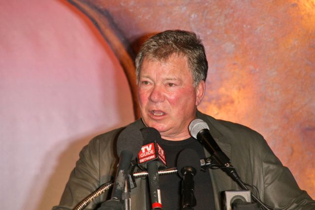 Actor William Shatner speaking at a podium with multiple microphones.