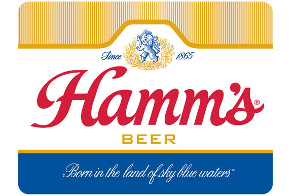 A classic red script "Hamm's" logo centered on a white background with a blue and gold crest above it. The bottom features a blue band with the slogan "Born in the land of sky blue waters" in white cursive.